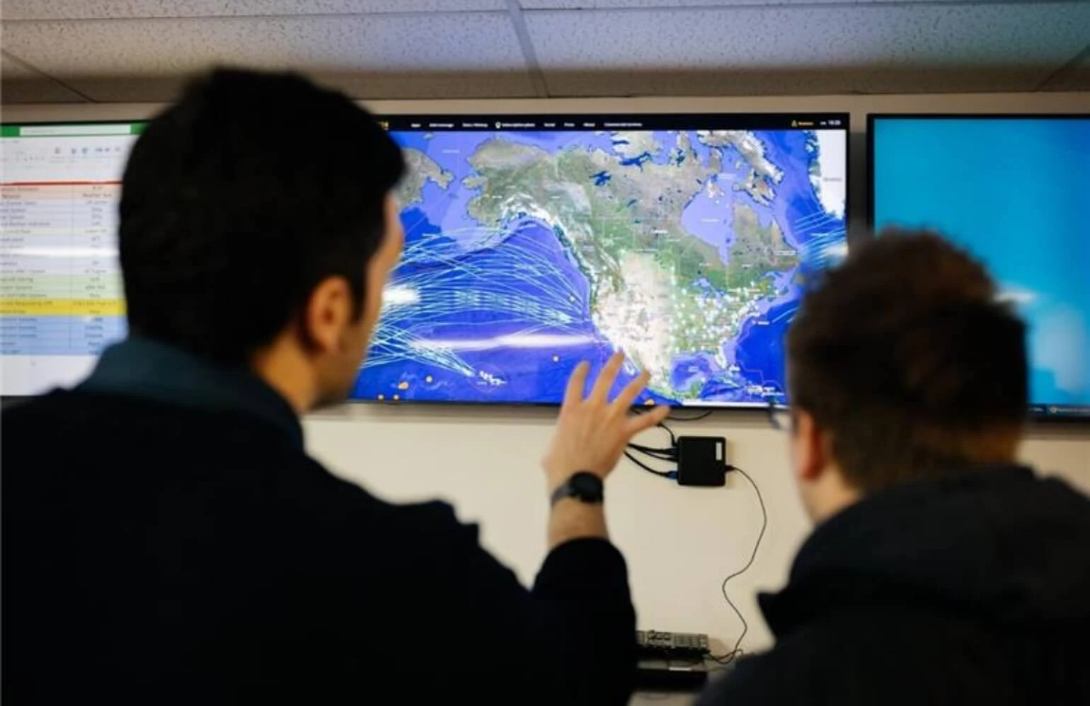 Two Flight Ops employees looking at flight patterns on a TV screen on the wall.