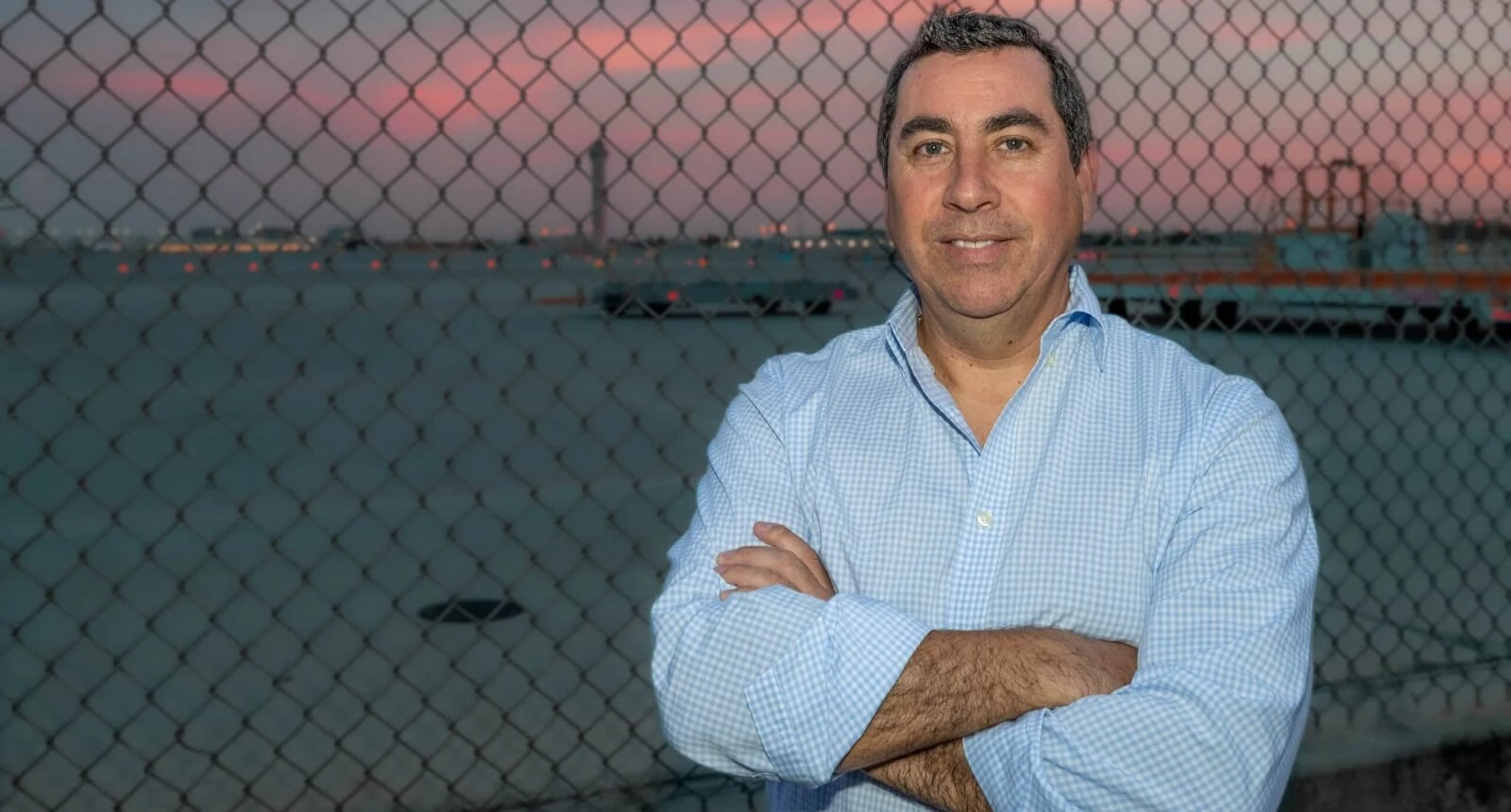 Photo of StratAir employee Jorge Corral standing in front of a chain link fence at the airport.