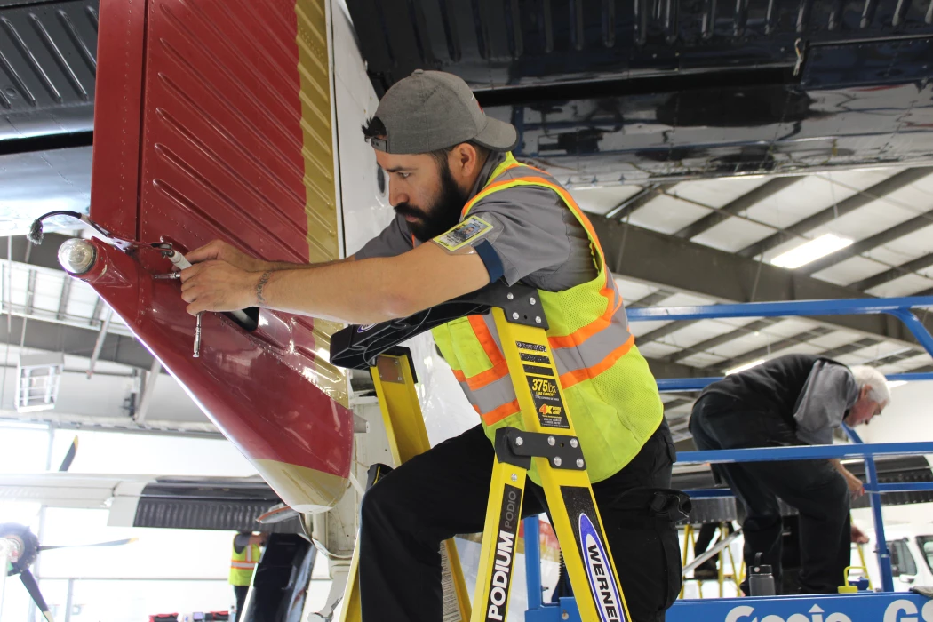 A NAMS mechanic standing on a ladder to fix a piece of the plane's wing.